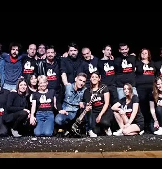 Grupo de personas en el escenario, pertenecientes a Peluts Productions, posando juntas después de una actuación de teatro o música en un ambiente de humor y memoria local.