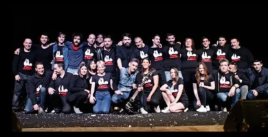 Grupo de personas en el escenario, pertenecientes a Peluts Productions, posando juntas después de una actuación de teatro o música en un ambiente de humor y memoria local.