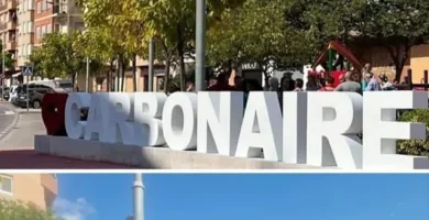 Gran letrero con la palabra 'CARBONAIRE' en una plaza arbolada en Carbonaire, rodeado de personas y vegetación urbana, destacando la participación comunitaria y el entorno cultural del vecindario.