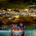Turistas disfrutando de un paseo en barca por el río subterráneo de las Coves de Sant Josep, rodeados de espectaculares formaciones rocosas y agua cristalina. Experiencia única en cueva natural, Castellón.