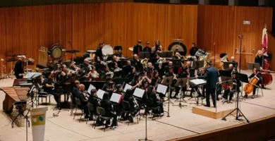 Concierto de la Unión Musical Vallduxense en un auditorio con una orquesta completa, instrumentos de viento y percusión, y un director al frente en Vall d’Uixó.